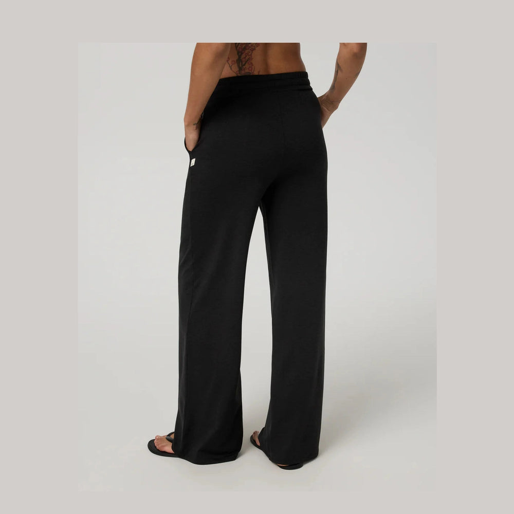 A person shown from the back wearing black Vuori Halo Essential Wideleg – Women's wide-leg pants with side pockets, standing against a light gray studio background.