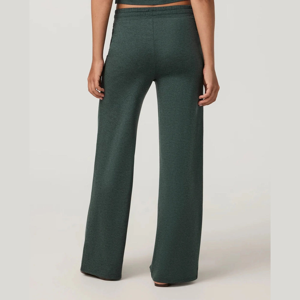 A person shown from the back wearing dark green wide-leg Vuori Halo Essential Wideleg – Women's pants against a plain light gray studio background.