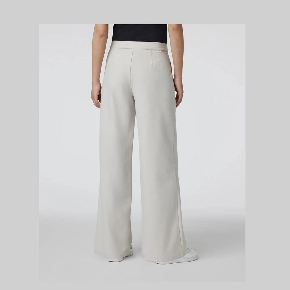 A model shown from the back wearing Vuori Elevation Trouser – Women's high-waisted, wide-leg trousers in a light cream or off-white color, paired with a black top and white sneakers, set against a plain light gray studio background.