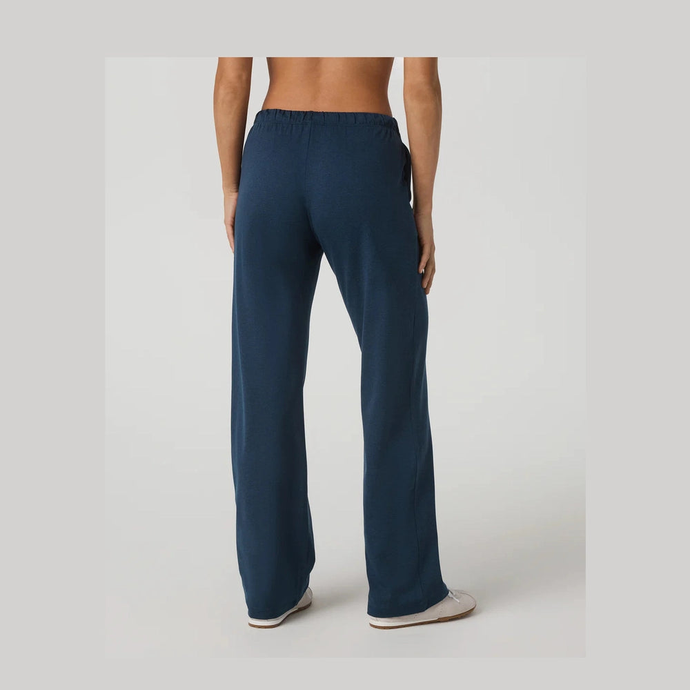 A person shown from the back wearing loose, wide-leg navy Vuori Halo Modern Straight Leg Pant – Women's pants and white slip-on shoes against a plain light gray studio background.
