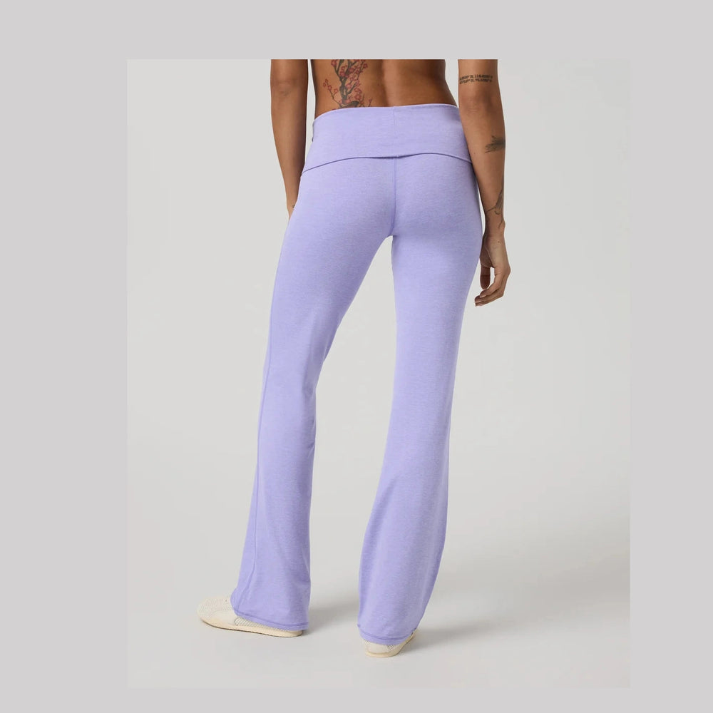 A person shown from the back wearing light lavender Vuori Halo Foldover Pant – Women's high-waisted flared pants, photographed against a plain light gray studio background.