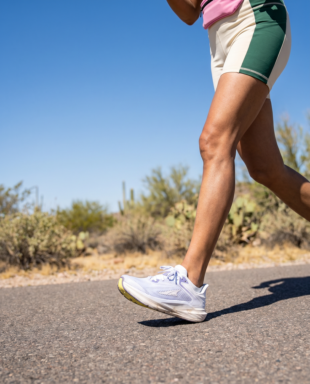 Person running on a road with a clear blue sky and desert landscape in the background