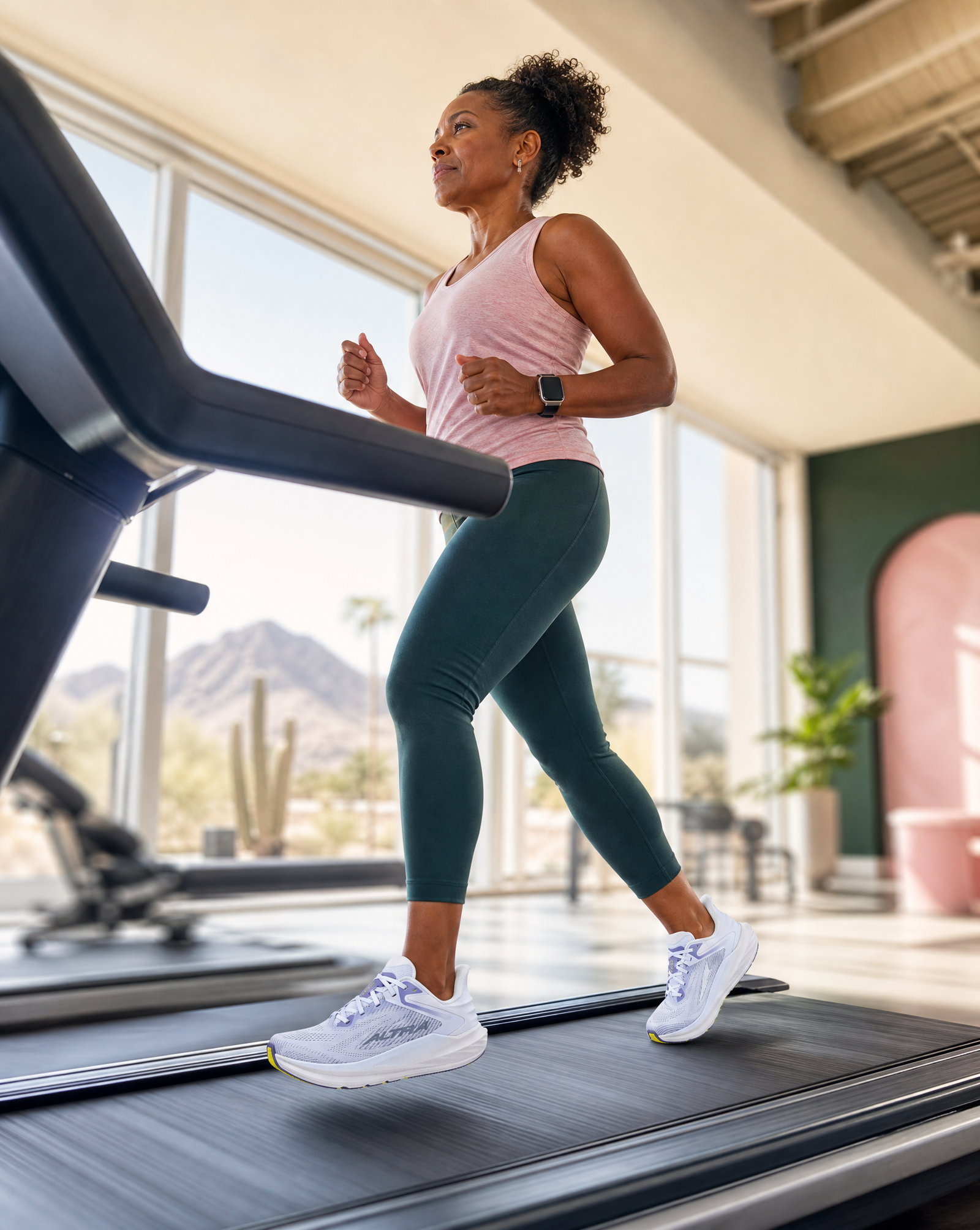 Woman running in an Altra Torin 8 shoe on a treadmill in a well-lit room with large windows.