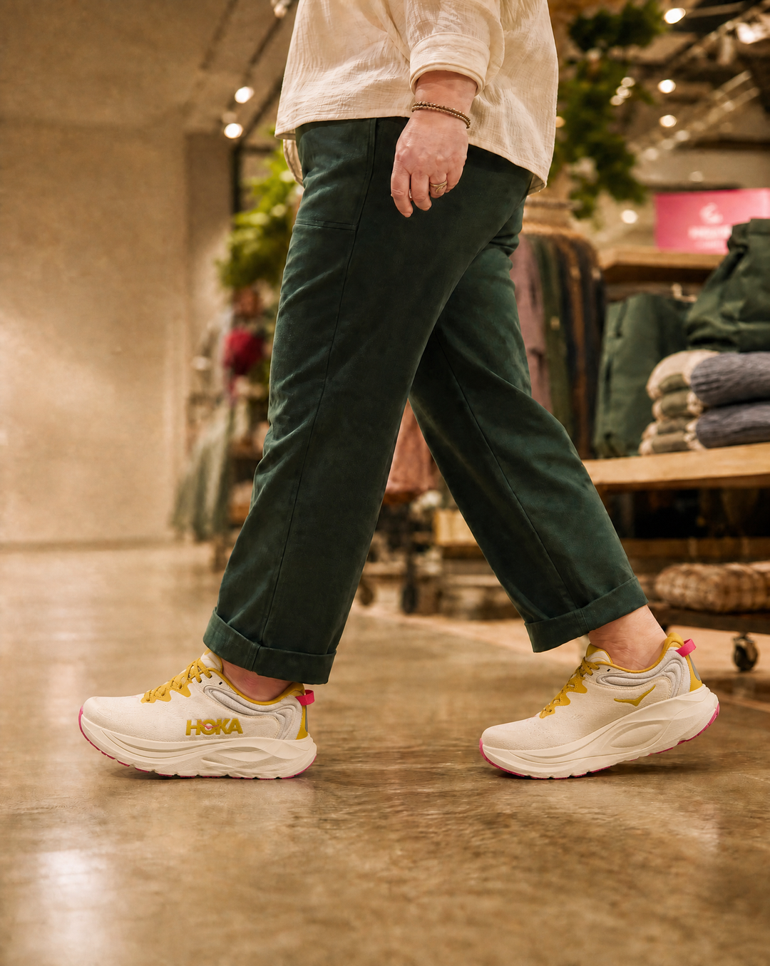 Person wearing green pants and Hoka Gaviota 6 sneakers with yellow accents in a store setting