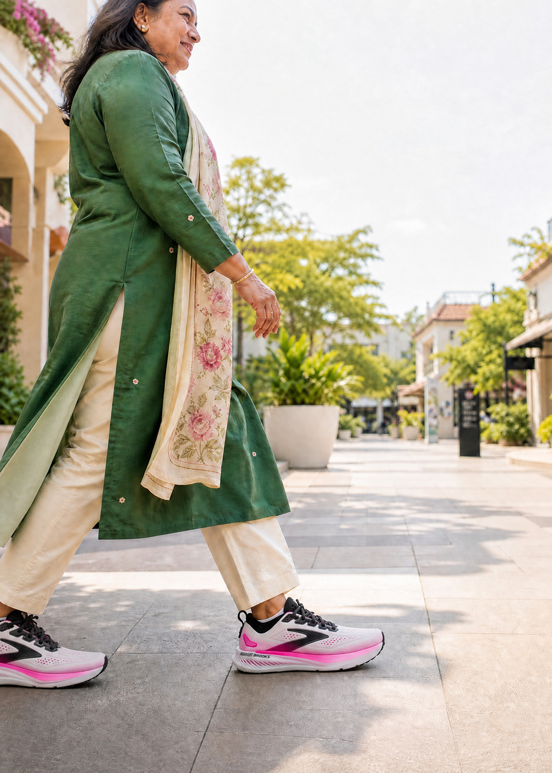 Woman walking outdoors wearing a green coat and pink Brooks Glycerin GTS 23 
sneakers.