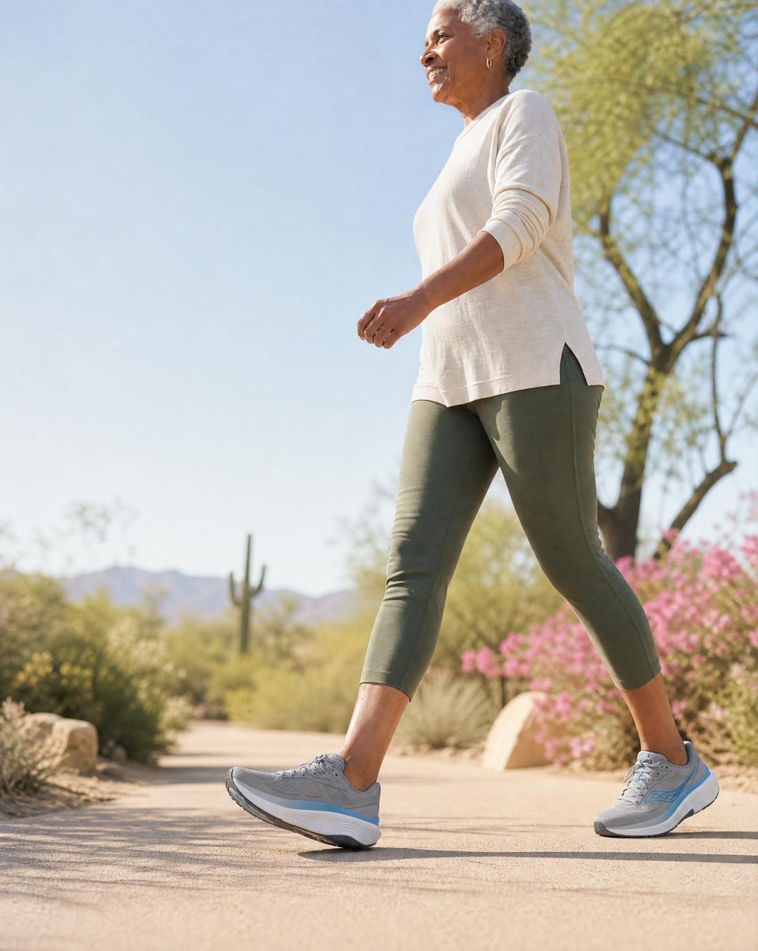 Woman walking on a path in a natural setting with trees and flowers.