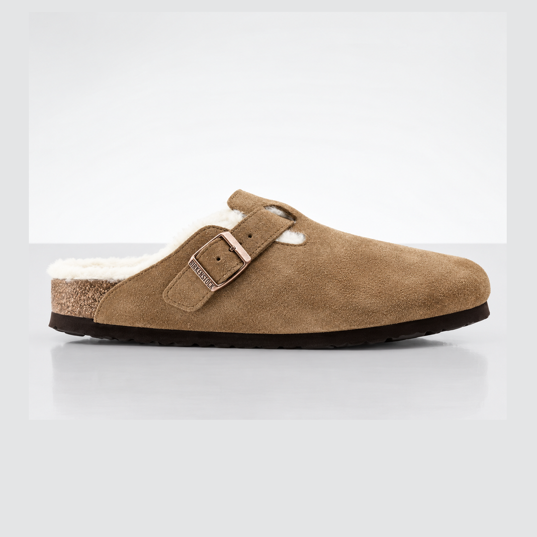 A single Birkenstock Boston Shearling tan suede clog slipper with a white shearling lining and a rose gold-tone buckle, shown from a side profile on a light gray background.