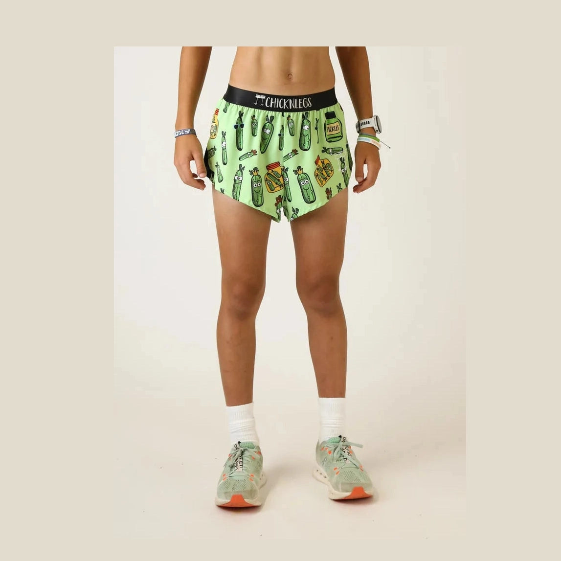 A person modeling light green Chicknlegs 2" Split Shorts – Men's with a colorful pickles print and a black waistband that reads 'CHICKLEGGS', shown from the waist down against a plain light background.