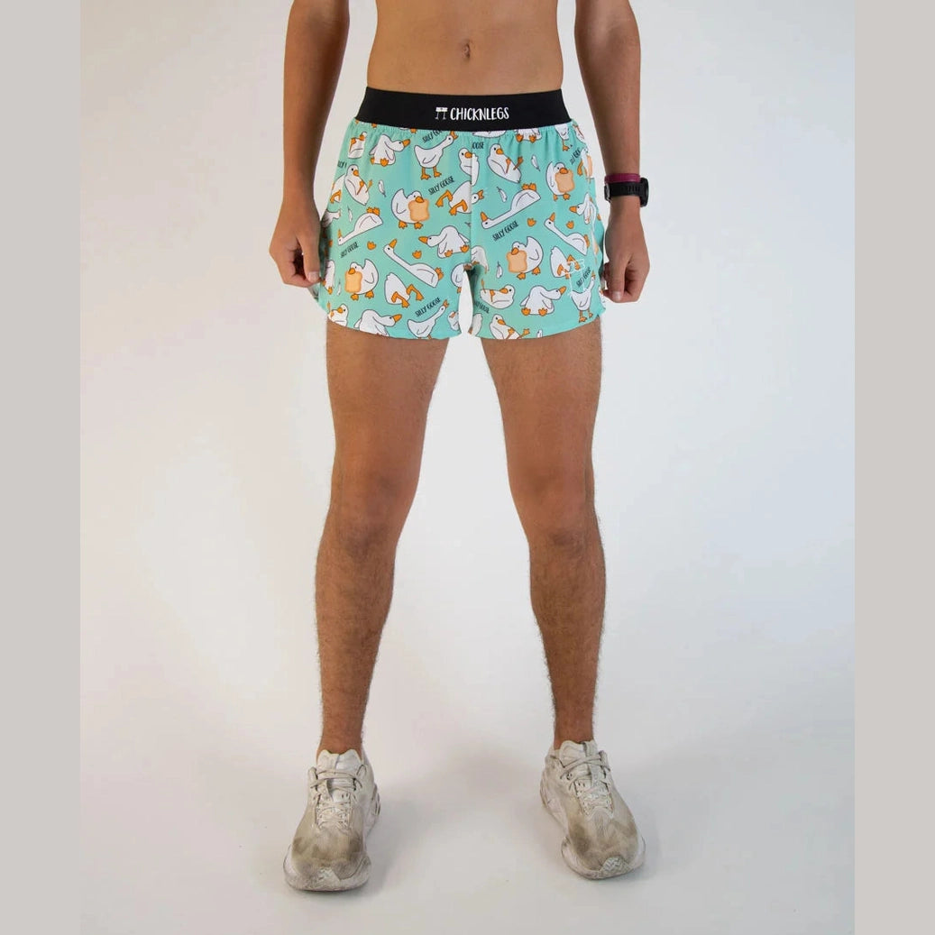 A person modeling light blue  Chicknlegs 2" Split Shorts – Men's with a cartoon dog print, a black waistband with the brand name 'Chicknlegs' visible, and white sneakers against a plain light background.