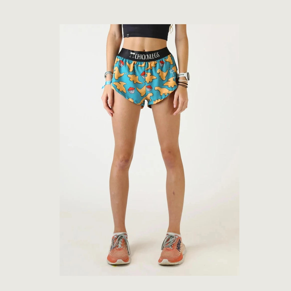 A model is shown from the waist down wearing colorful Chicknlegs 1.5" Split Shorts – Women's with a blue, yellow, and red pattern, featuring the brand name 'Chicknlegs' on the black waistband.