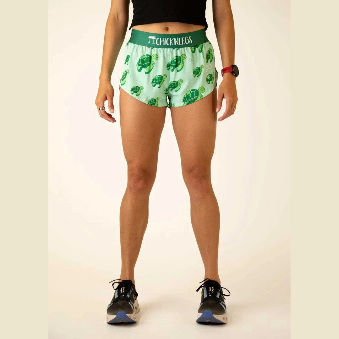 Person wearing green Chicknlegs 1.5" Split Shorts – Women's shorts with turtle pattern on a plain background