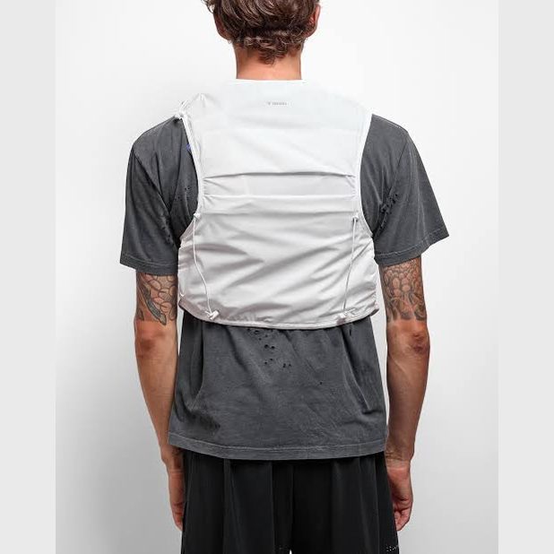 Rear view of a man wearing a light gray Justice Cordura 5L Hydration Vest over a dark gray t-shirt and black shorts, against a plain white studio background.