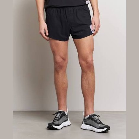 A person wearing black Space-O Shorts--Men's and dark gray running shoes, shown from the waist down against a plain light gray studio background.