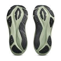 A pair of athletic shoe soles shown from the bottom, featuring a light sage green base with black textured tread patterns, set against a plain white background.