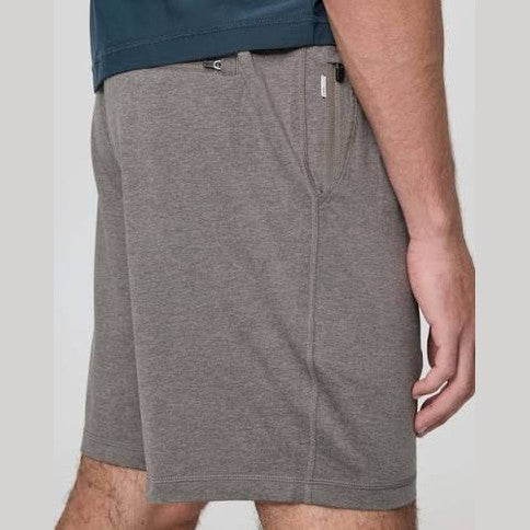 A close-up of a person wearing heather gray Vuori Ponto Short – Men's  athletic shorts with a side zipper pocket and a dark blue top partially visible at the top edge.