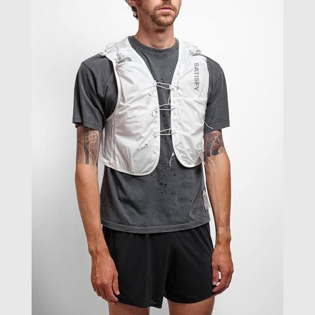 A man wearing a white Justice Cordura 5L Hydration Vest over a dark gray t-shirt and black shorts, standing against a light gray studio background.