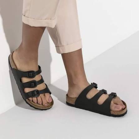 Black sandals worn with beige pants on a white background