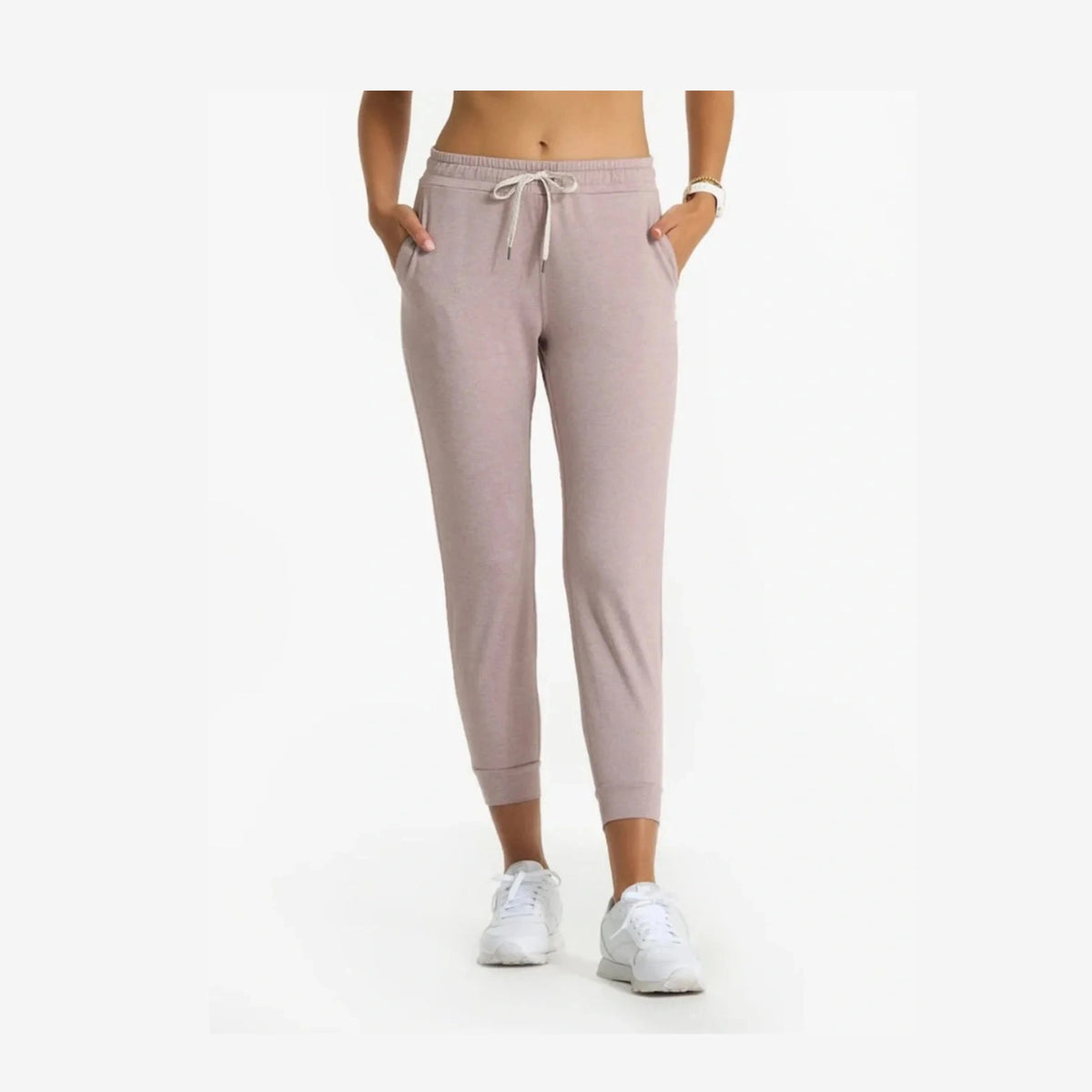 A person wearing light dusty pink Vuori Performance Jogger – Women's jogger sweatpants with a white drawstring, paired with white sneakers, shown from the waist down against a plain white background.
