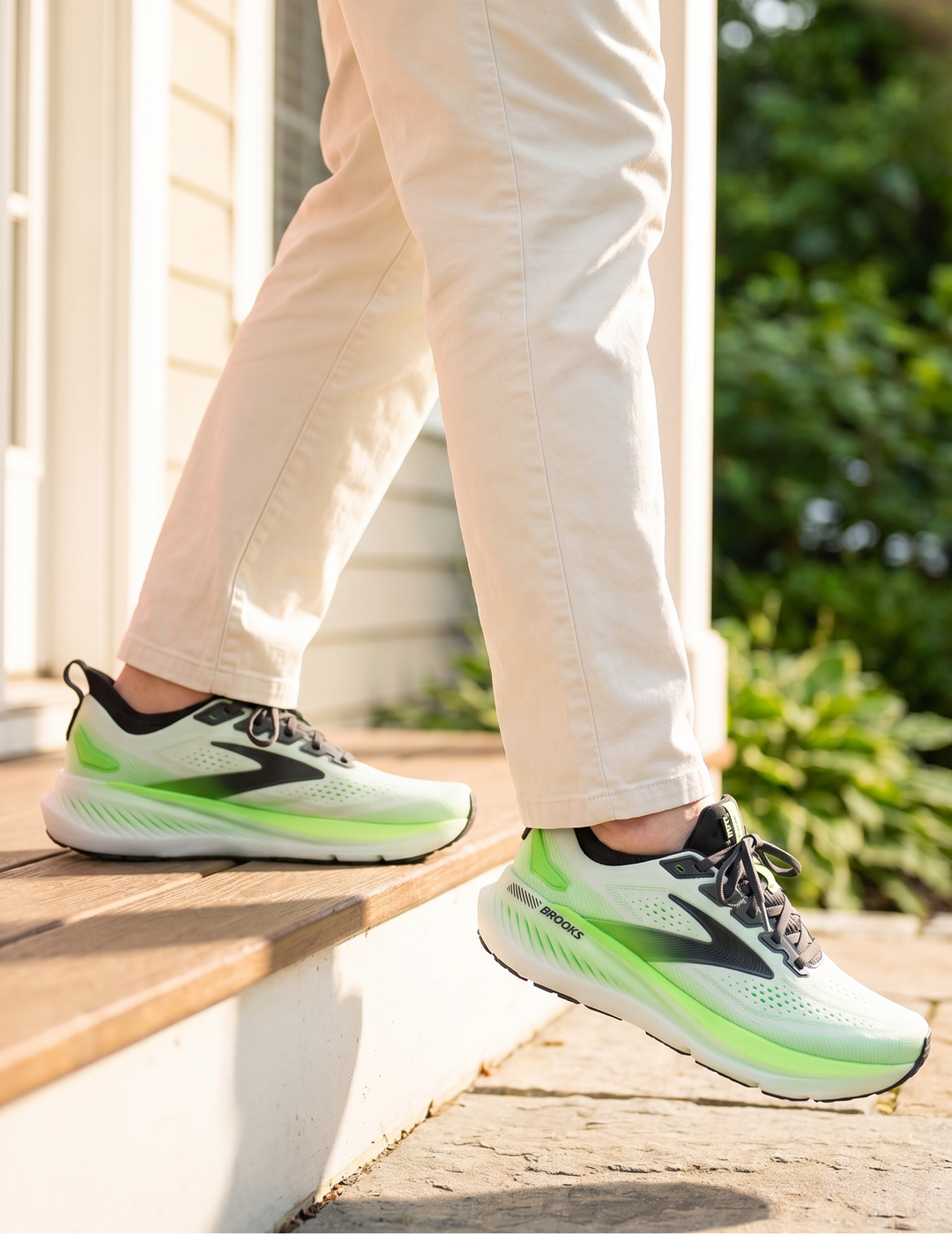 Person wearing green and black Brooks Glycerin GTS 23 sneakers stepping onto a wooden deck.