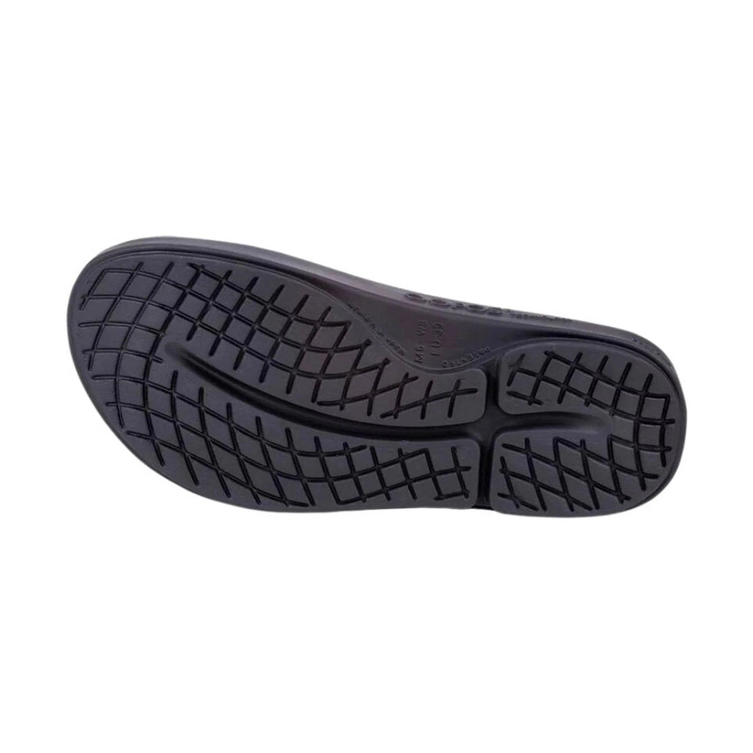 The black rubber outsole of a shoe, showing a detailed tread pattern, photographed from a top-down view on a solid white background.