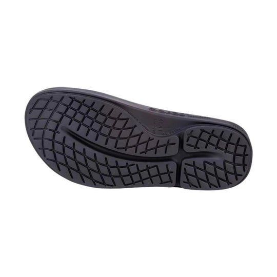 The black rubber outsole of a shoe, showing a detailed tread pattern, photographed from a top-down view on a solid white background.