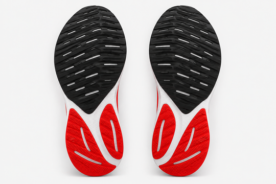 A top-down view of a pair of athletic shoe soles, showing a black textured outsole with white striping and a red and white heel section, set against a plain light gray background.