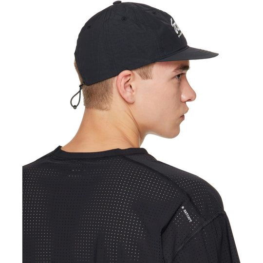 A man in profile wearing a black Flitesilk 5 Panel Pinch Cap with a white embroidered logo and a black mesh athletic shirt, photographed against a solid white background.