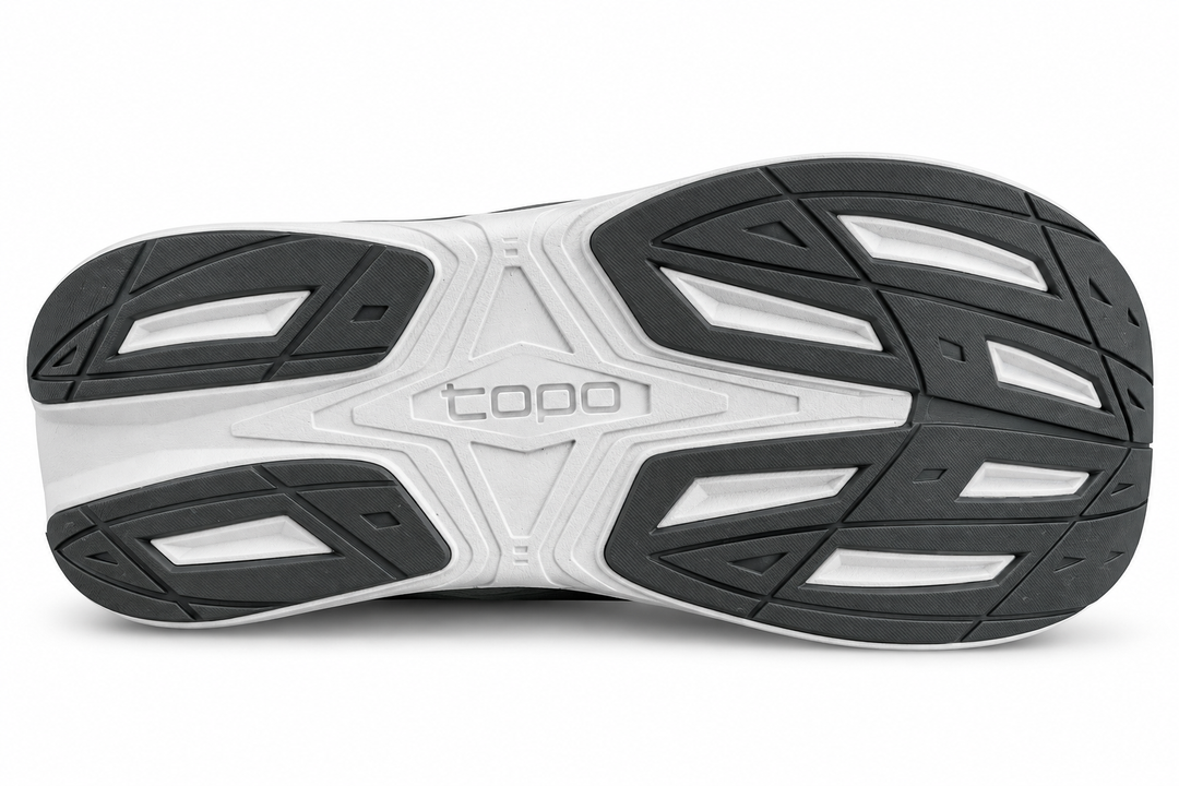 The outsole of a shoe shown from a top-down view, featuring a white and black tread pattern with the brand name &