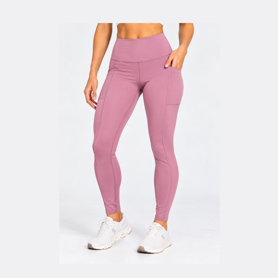 A model wearing high-waisted, form-fitting Purestretch 7" Tight Shorts in a dusty rose pink color with side pockets, paired with white sneakers, against a plain white studio background.