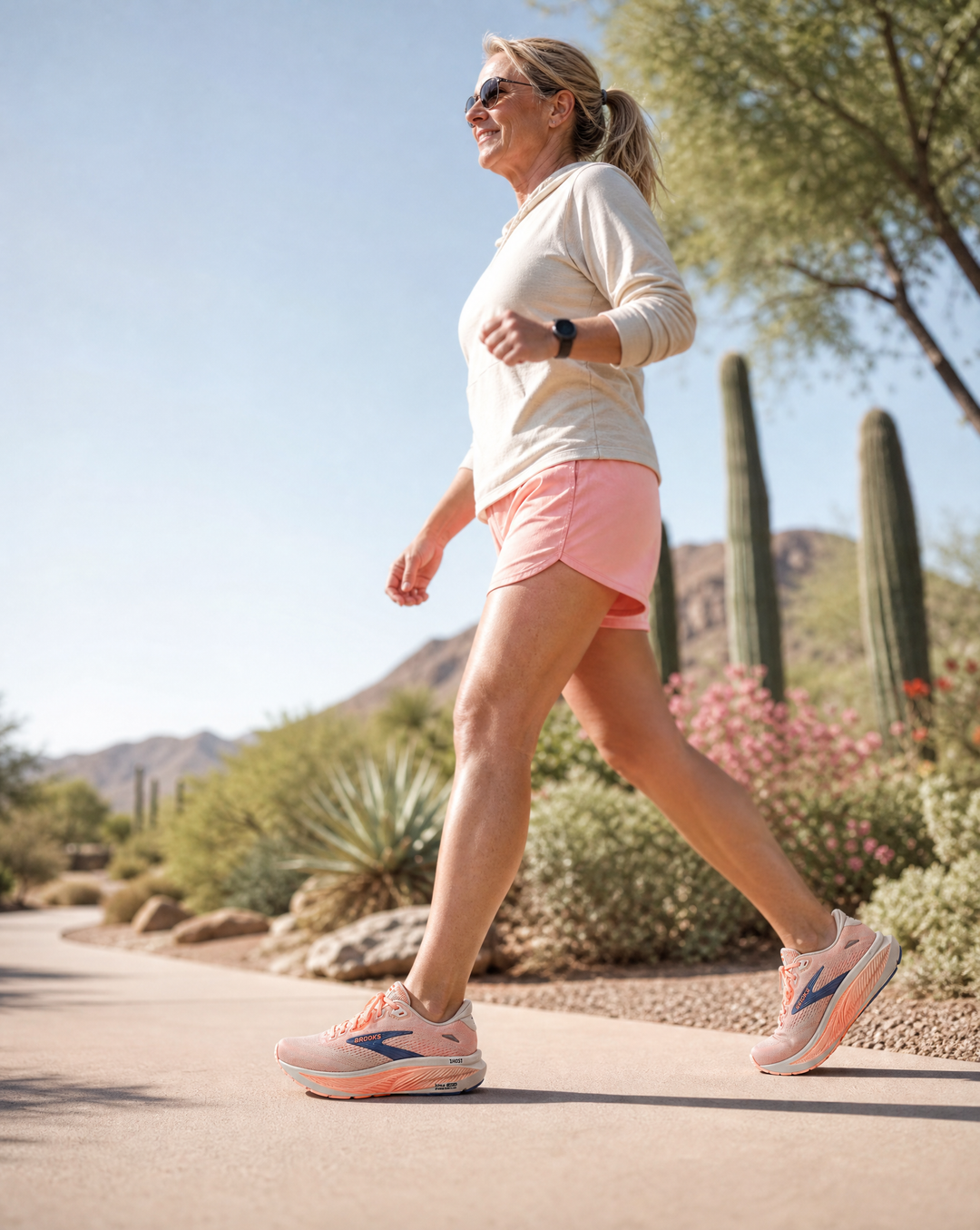 Woman walking outdoors in the Brooks Ghost 18 in a desert-like setting with cacti and mountains in the background.