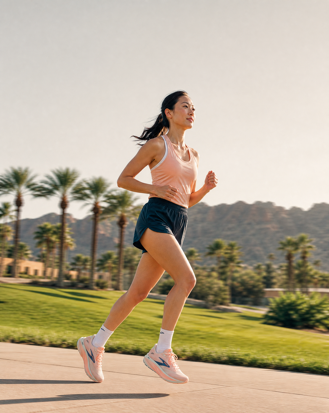 Woman running in Brooks Ghost 18 on a path with palm trees and mountains in the background