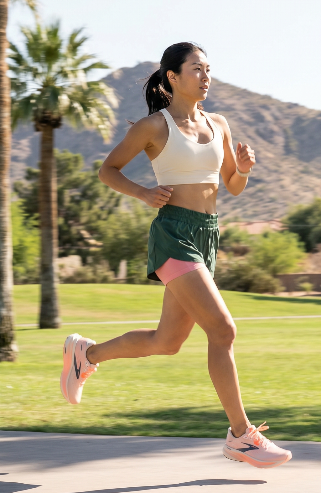 Woman running on a path with palm trees and mountains in the background wearing the Brooks Ghost 18 shoe